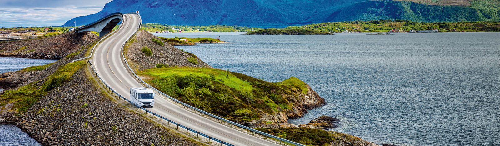 Witte camper op een kustweg langs fjorden en groene eilanden